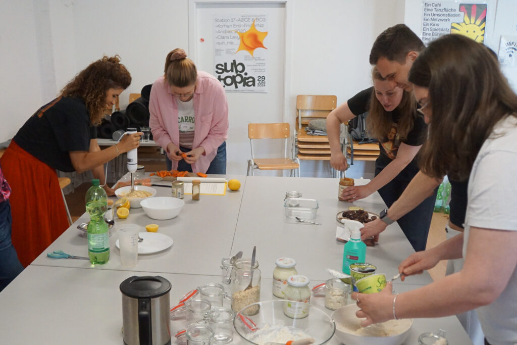 Gesunde Snacks zubereiten Mehrere Personen stehen verteilt um aneinandergereihte Tische und bereiten sichtlich erfreut und konzentriert gesunde Snacks zu.